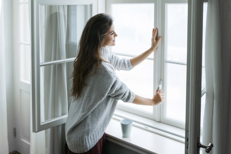 Female homeowner opening window for cool air after air handler broke down.