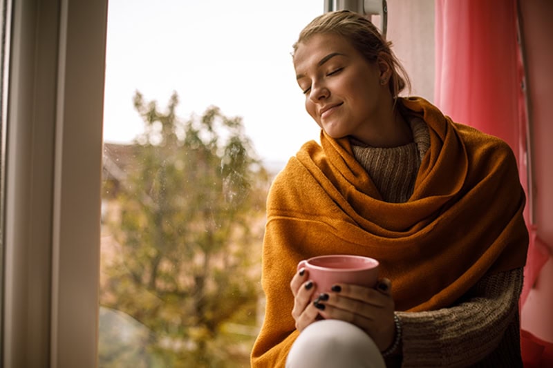 Woman looking cozy with a mug in hand as she looks at the fall view.